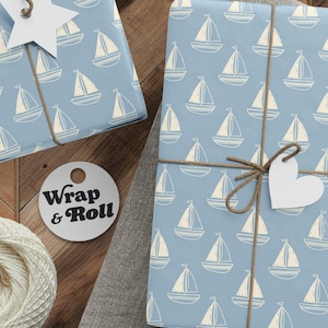 May include: Two rectangular gifts wrapped in light blue paper with a repeating white sailboat pattern, tied with brown twine. One gift features a white star-shaped tag, the other a heart-shaped tag. Includes a ball of white yarn and scissors.