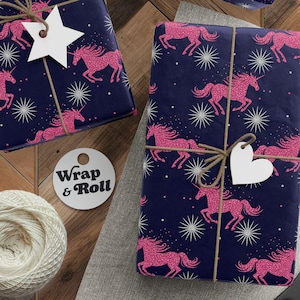 Puede incluir: Regalos envueltos en papel azul marino con diseños de unicornios rosas y estrellas blancas. Cada paquete está atado con hilo y una etiqueta decorativa. También se ven un carrete de hilo, tijeras y etiquetas.