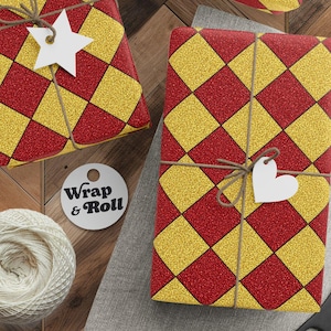 Puede incluir: Regalos envueltos con papel a cuadros rojo y amarillo, atados con hilo y etiquetas blancas en forma de estrella. También hay un carrete de hilo, tijeras y etiquetas. La etiqueta redonda dice "Wrap & Roll".