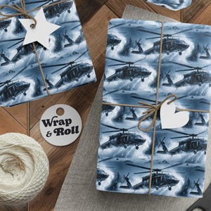 Puede incluir: Papel de regalo con un patrón repetido de helicópteros negros sobre un fondo azul y blanco. Los regalos envueltos están atados con hilo y adornados con etiquetas blancas en forma de estrella y corazón. También hay un carrete de hilo, tijeras y una etiqueta que dice "Wrap & Roll".
