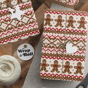 Puede incluir: Regalos envueltos en papel con estampado de hombre de jengibre, atados con hilo y etiquetas blancas. También se ven un carrete de hilo, tijeras y una etiqueta con "Wrap & Roll".