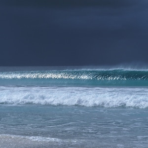 Könnte beinhalten: Eine große Welle bricht an einem Sandstrand, mit einem dunklen, stürmischen Himmel darüber. Das Wasser ist tiefblau, mit weißem Schaum an der Welle.