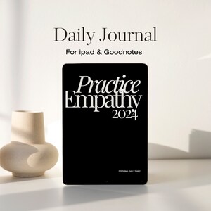 Könnte beinhalten: Ein schwarzer digitaler Planer mit weißem Text, der "Practice Empathy 2024" und "Personal Daily Diary" lautet. Der Planer befindet sich auf einer weißen Oberfläche mit einer beigefarbenen Vase.