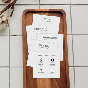 Puede incluir: Un conjunto de tarjetas cuadradas blancas con texto en negro para una guía de estudio bíblico. Las tarjetas están etiquetadas con los encabezados PRAYER, APPLICATION, OBSERVATION, SCRIPTURE y BIBLE STUDY GUIDE con el acrónimo S.O.A.P.