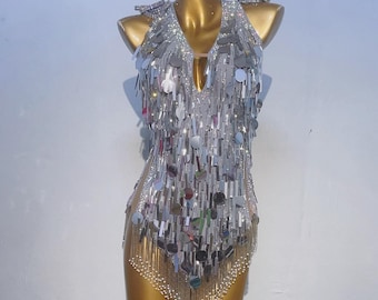 May include: A silver sequined bodysuit with fringe and a V-neckline. The bodysuit is on a mannequin.