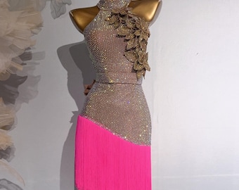 Può includere: Un abito da ballo scintillante di colore marrone chiaro con scollo halter e gonna a frange rosa. L'abito è decorato con accenti di foglie dorate.