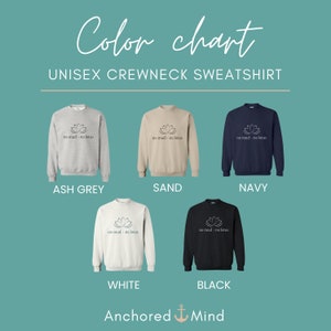 Op de afbeelding: Kleurenkaart voor een unisex crewneck sweatshirt in asgrijs, zand, marine, wit en zwart. Het sweatshirt heeft een lotusbloem grafiek met de tekst "no mud - no lotus".