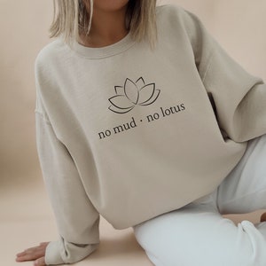 May include: A beige sweatshirt with a black lotus flower graphic and the text "no mud. no lotus" printed on the front.