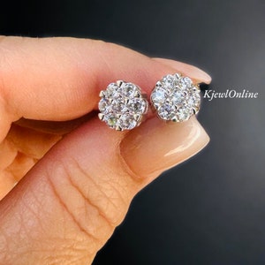 May include: A pair of silver stud earrings with a cluster of small, clear cubic zirconia stones. The earrings are set in a round shape and have a polished finish.