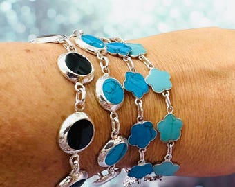 May include: A set of four silver bracelets with turquoise and black stones. The bracelets feature round and flower-shaped stones.