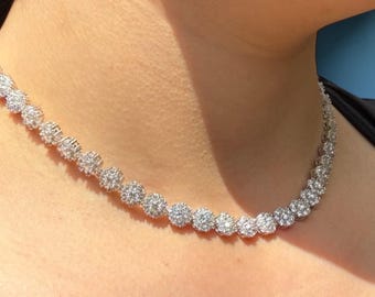 May include: A sparkling necklace with multiple round, clustered, clear gemstones. The necklace is worn around the neck, with the gemstones catching the light. The necklace appears to be made of silver or a similar metal.