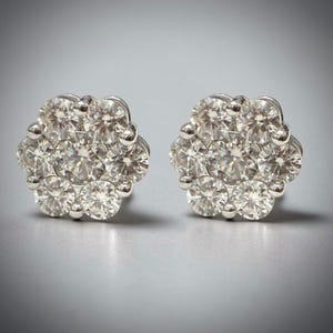May include: A pair of diamond cluster stud earrings. Each earring features a floral design with multiple round-cut diamonds set in a silver-colored metal. The earrings are displayed against a gray background.