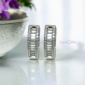 May include: A pair of silver hoop earrings with a row of baguette-shaped diamonds set in a channel setting.
