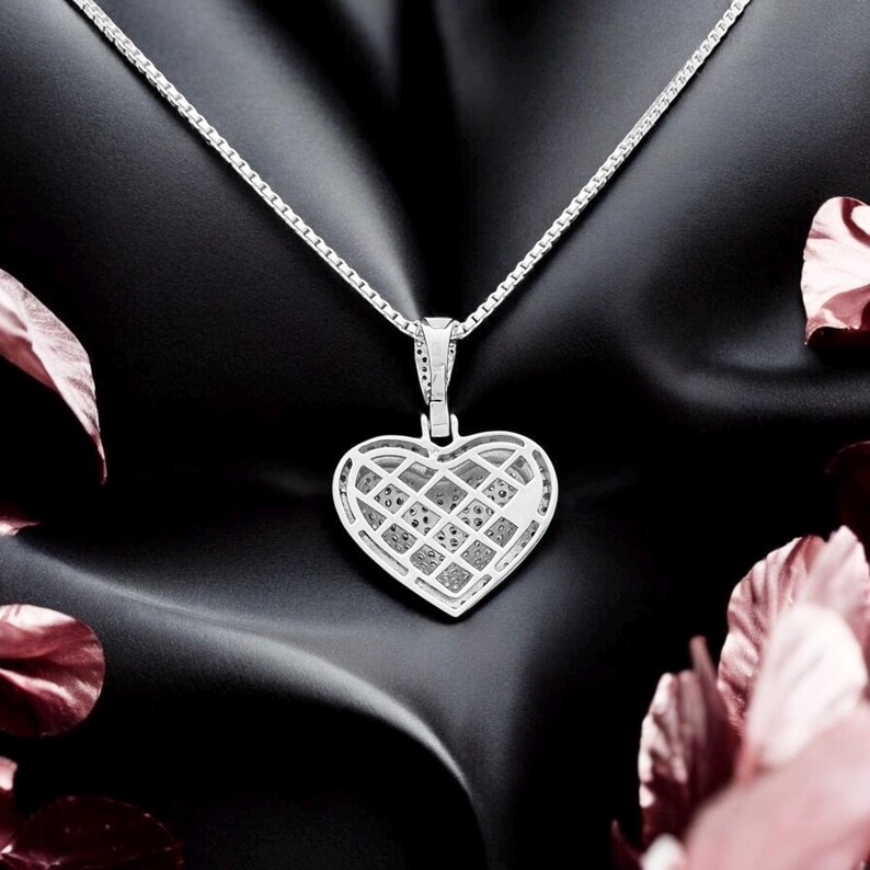 May include: A silver heart-shaped pendant necklace with a diamond-like pattern. The pendant hangs from a delicate chain. The background is black with pink floral accents.