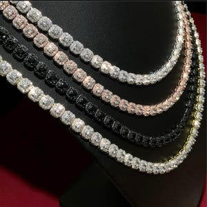 May include: Four layered tennis necklaces featuring square-cut stones in silver, rose gold, and black metal settings. Each chain is composed of a continuous row of sparkling, faceted stones, creating a uniform and reflective appearance across all pieces.