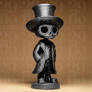 May include: A black figurine of a skeleton wearing a top hat and a long coat. The skeleton has detailed facial features, including eye sockets and a skull-shaped face. The figurine is standing on a round base.