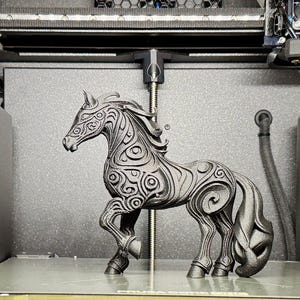 Puede incluir: Una figura decorativa de caballo negro con intrincados patrones de remolinos, dentro de una impresora 3D. El caballo tiene una melena y cola fluidas, y est&aacute; posado de forma din&aacute;mica. El fondo es gris oscuro.