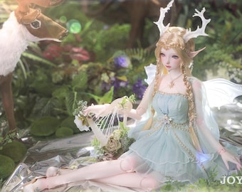 May include: A porcelain doll with blonde hair and a light blue dress, wearing a crown of antlers and fairy wings. The doll is holding a harp and sitting in a woodland setting.