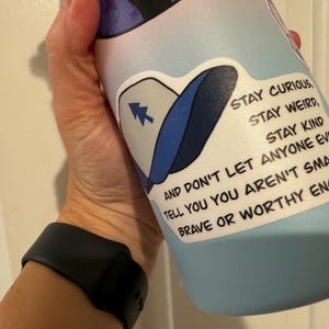 May include: A blue water bottle with a white sticker that says "STAY CURIOUS, STAY WEIRD, STAY KIND AND DON'T LET ANYONE EVER TELL YOU YOU AREN'T SMART OR BRAVE OR WORTHY ENOUGH."