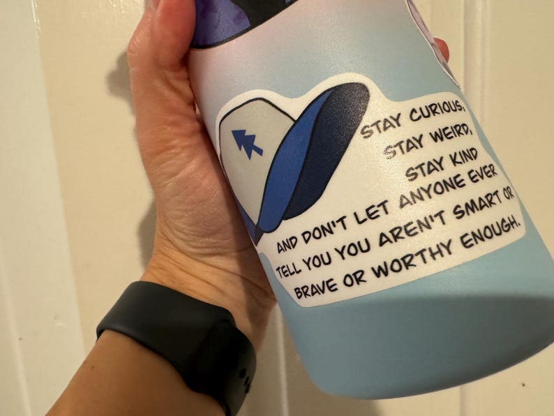 May include: A blue water bottle with a white sticker that says "STAY CURIOUS, STAY WEIRD, STAY KIND AND DON'T LET ANYONE EVER TELL YOU YOU AREN'T SMART OR BRAVE OR WORTHY ENOUGH."