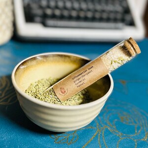 Puede incluir: Un tubo de ensayo de vidrio lleno de semillas de hinojo y una etiqueta de papel marrón que dice "Inflammation Soak Ginger/Bergamot Turmeric Fennel".