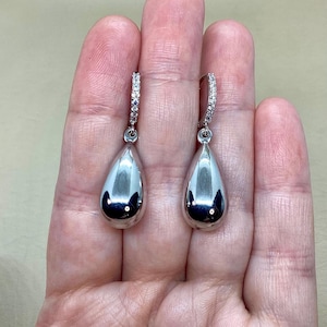 May include: A pair of silver teardrop earrings with a small row of clear stones around the top of the hoop.