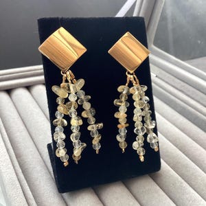 May include: Gold dangle earrings with a square top and a long strand of light brown and clear faceted beads.