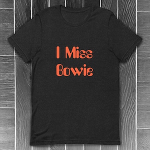Könnte beinhalten: Schwarzes T-Shirt mit dem Text "I Miss Bowie" in Orange.