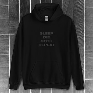 以下が含まれることがあります： 前面に「SLEEP DIE GOTH REPEAT」という文字が白でプリントされた黒いフード付きスウェットシャツです。