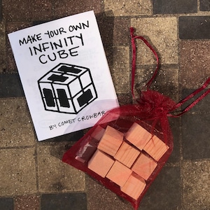 Puede incluir: Una bolsa de malla roja llena de bloques de madera, y un papel blanco con el texto "Make Your Own Infinity Cube" y "By Comet Crowbar".