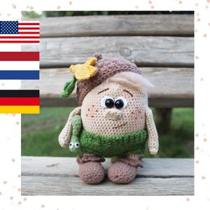 Puede incluir: Un juguete de peluche tejido a crochet con forma de persona con un sombrero marrón, una camisa verde y zapatos marrones. El juguete sostiene un gusano verde en su mano.