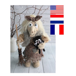 May include: A handmade crochet witch doll with a long nose, holding a black cat and a broom. The witch has white hair, a brown bow, and is wearing a brown and tan dress. The cat has white whiskers and a white chest.