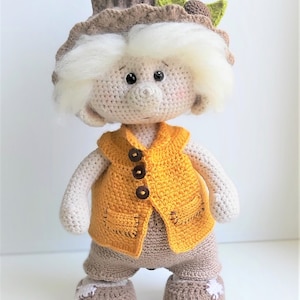 May include: A crocheted doll with white hair, a brown hat with a green leaf, a yellow vest with brown buttons, and brown pants and shoes.