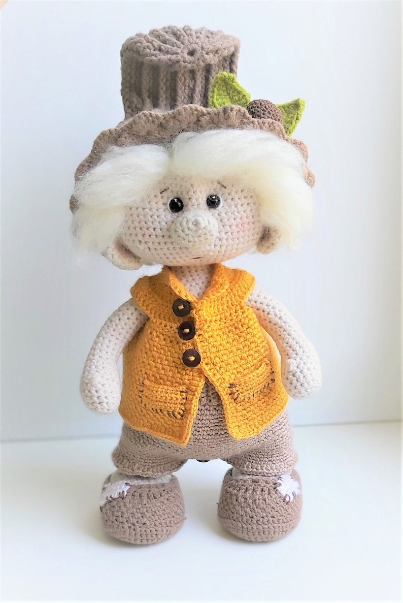 May include: A crocheted doll with white hair, a brown hat with a green leaf, a yellow vest with brown buttons, and brown pants and shoes.