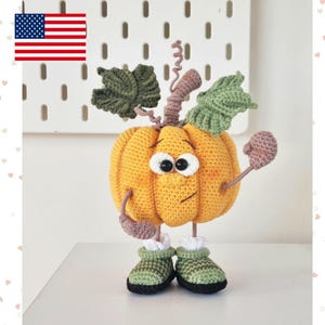 May include: A crocheted pumpkin figure with a bright orange body, two green leaves, and a brown stem. The figure has large white eyes with black pupils, thin brown arms with small hands, and wears green textured boots with white cuffs.