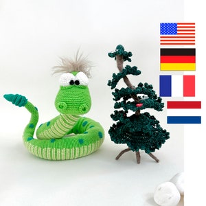 Op de afbeelding: Een groene gehaakte slang met witte ogen en een groene gehaakte boom met een bruine stam. De slang is opgerold in een cirkel en de boom staat rechtop.