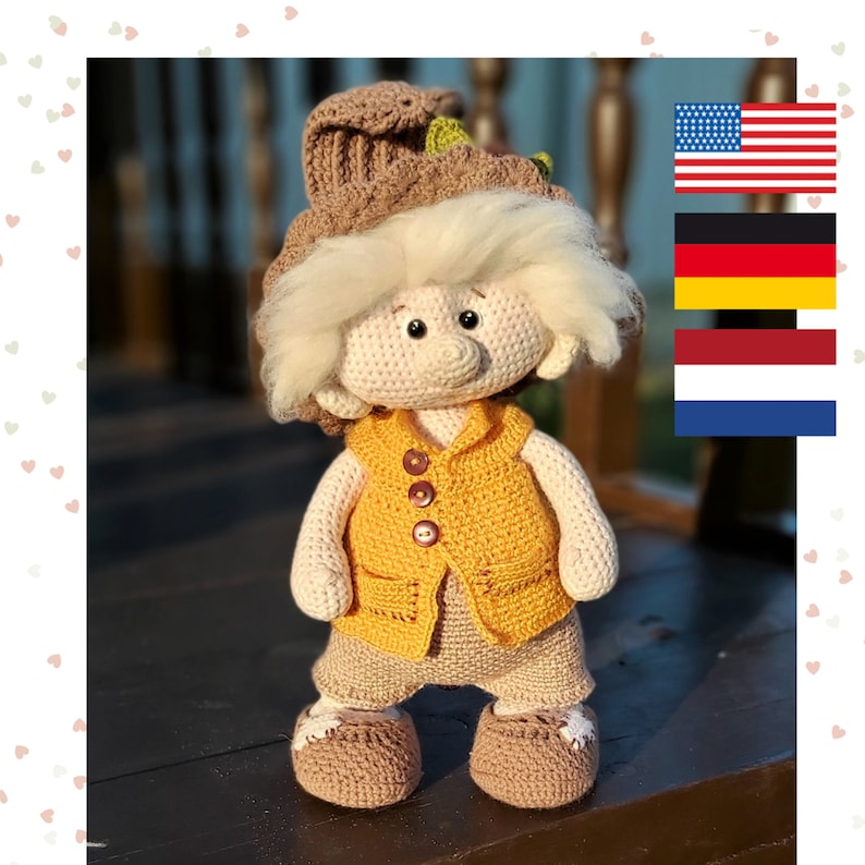 May include: A crocheted doll with blonde hair, wearing a brown hat, a yellow vest, and brown pants. The doll is standing on a wooden surface.