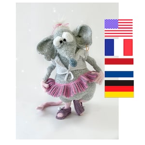 May include: A gray crocheted mouse wearing a pink tutu and sandals. The mouse has large, round eyes and a pink bow in its hair. The mouse is standing on a white background.