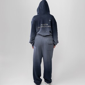 May include: A two-piece matching set of a hooded sweatshirt and sweatpants in a gradient blue color. The back of the hoodie has the text "we collide shattering my mind" with star graphics. The sweatpants have a single pocket on the back.