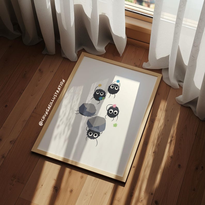 May include: A framed art print featuring a whimsical illustration of soot sprites with colorful accents and rocks. The artwork is set against a white background, with the artist's name in the lower left corner. The frame is a light brown color.