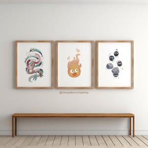 May include: Three framed art prints featuring illustrations of a dragon, a fire spirit, and soot sprites. The dragon is depicted in shades of blue, pink, and white. The fire spirit is orange and yellow. The soot sprites are black with party hats.