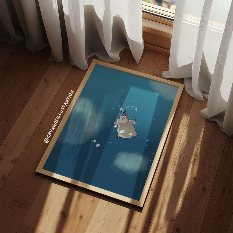 May include: A framed art print featuring a whimsical illustration of a hippo floating in a blue space with clouds. The hippo has a small bird on its head. The frame is light brown, and the artwork is set against a wooden floor.