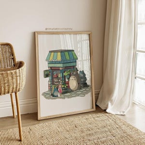 May include: A framed illustration featuring a whimsical shop scene with characters reminiscent of a popular animated film. The artwork showcases a shop with a striped awning, a large, furry creature, and two smaller figures. The frame is light-colored.