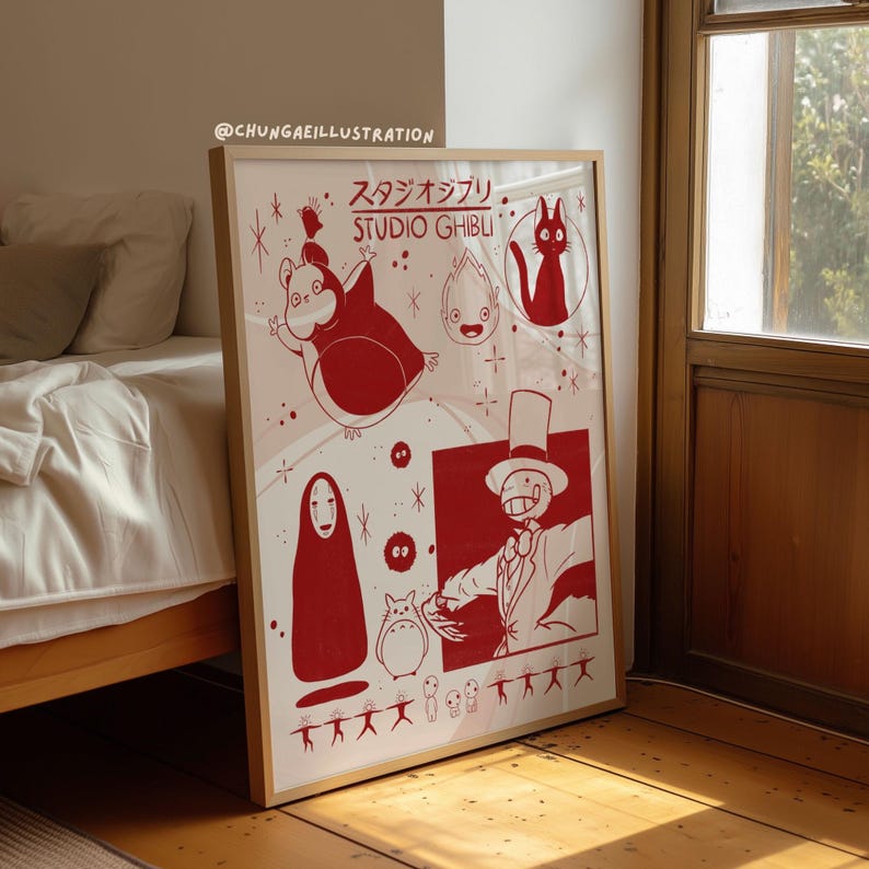 May include: A framed Studio Ghibli art print featuring red illustrations of characters from various animated films. The print includes characters like Totoro, No-Face, and a cat, with Japanese text and the Studio Ghibli logo. The frame is a light brown color.