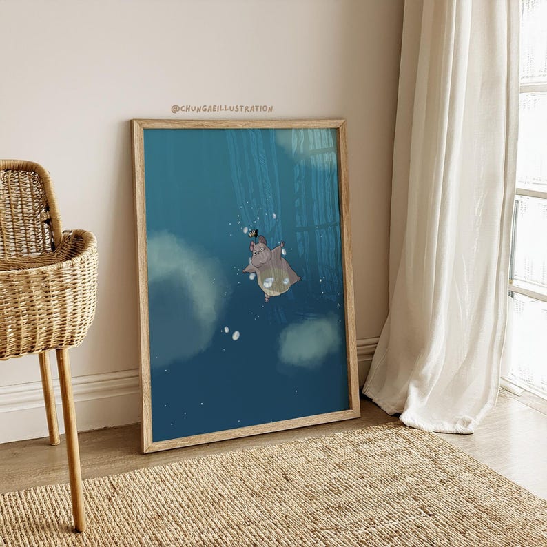 May include: A framed art print depicting a cartoon hippo floating in a blue underwater scene. The hippo wears a hat and cape. The print is in a wooden frame. The artwork is displayed on a wall, next to a window with white curtains.