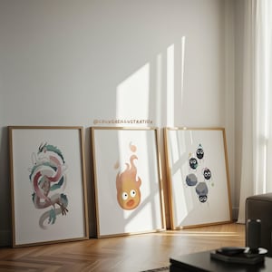 May include: Three framed art prints leaning against a white wall. The prints feature watercolor illustrations of a dragon, a flame, and soot sprites. The frames are a light wood color, and the artwork is on white backgrounds.