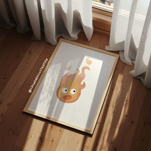 May include: A framed art print featuring a cartoon fire spirit with a surprised expression. The artwork is primarily orange and yellow, set against a white background, and framed in light wood. The artist's name is visible in the corner.