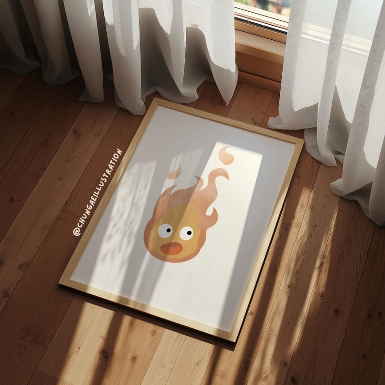 May include: A framed art print featuring a cartoon fire spirit with a surprised expression. The artwork is primarily orange and yellow, set against a white background, and framed in light wood. The artist's name is visible in the corner.