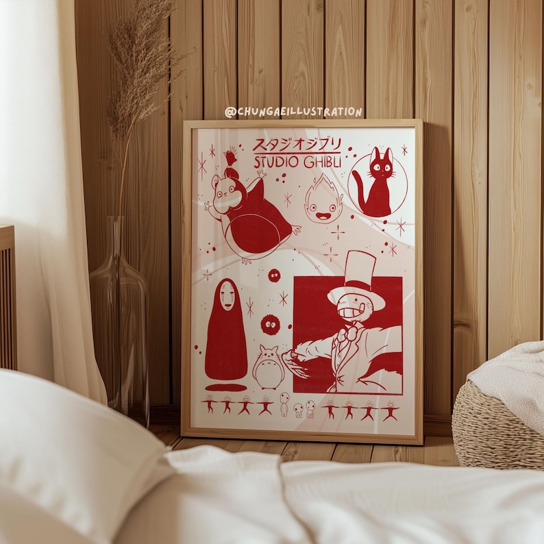 May include: A framed art print featuring red illustrations of characters from Studio Ghibli films. The print includes characters like Totoro, a cat, and a faceless spirit, set against a white background. The frame is a light brown color.