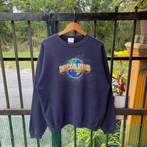 May include: A navy blue sweatshirt with a graphic of a globe and the text "Universal Studios Japan" printed on the front.